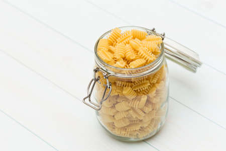 Raw radiatori pasta on a glass jar on blue wood tableの写真素材