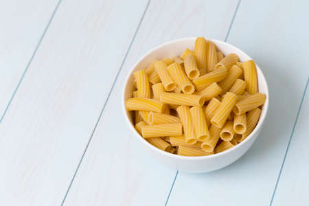 Raw tortiglioni pasta in a white bowl on blue wood tableの写真素材