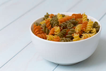 Raw fusilli pasta in a white bowl on blue wood tableの写真素材