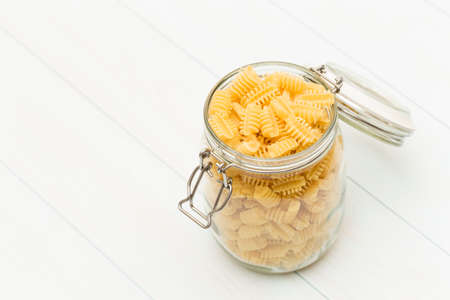 Raw radiatori pasta on a glass jar on blue wood tableの写真素材