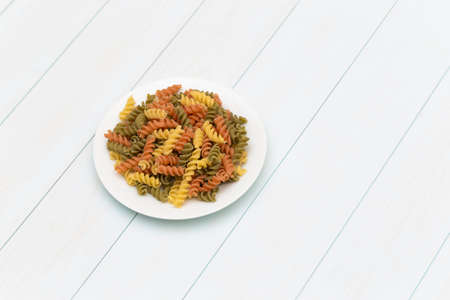 Raw fusilli pasta in a white plate on blue wood tableの写真素材