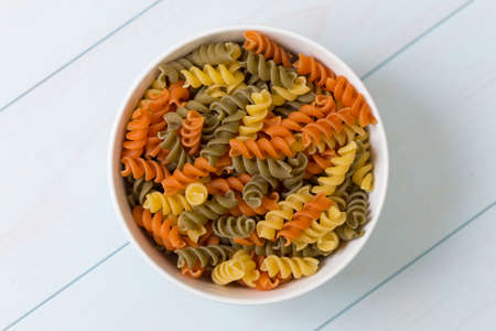 Raw fusilli pasta in a white bowl on blue wood tableの写真素材