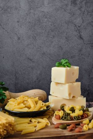 Different raw uncooked Italian pasta with cheese on wooden table against dark background. Diet and food concept. Copy space.の写真素材