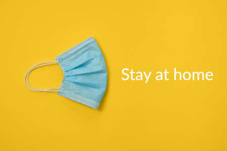 COVID-19 disposable surgical face mask on yellow background. Protection against coronavirus and epidemic. Medical concept with "stay at home" textの写真素材