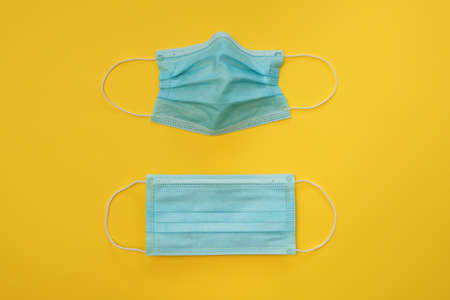 COVID-19 two disposable surgical face masks on yellow background. Protection against coronavirus and epidemic. Medical conceptの写真素材