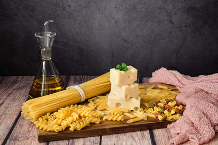 Different raw uncooked Italian pasta with cheese and olive oil on wooden table against dark background. Diet and food concept. Copy space.の写真素材