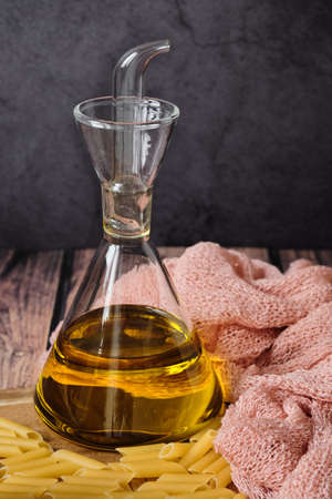 Raw uncooked Italian pasta with olive oil on wooden table against dark background. Diet and food concept. Copy space.の写真素材
