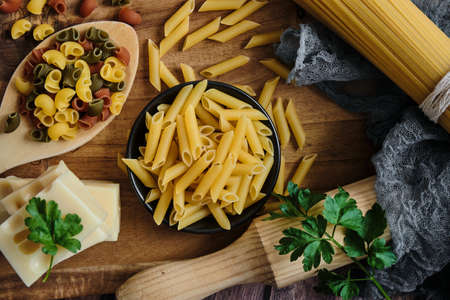 Different raw uncooked Italian pasta and cheese on wooden table. Diet and food concept. Flat lay,...
