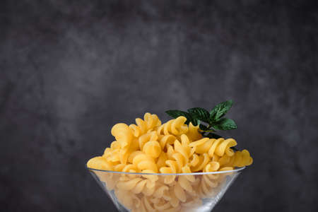 Raw uncooked italian pasta on cocktail glass over white marble. Fusilli. Diet and food concept. Copy space.の写真素材