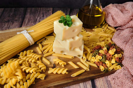 Different raw uncooked Italian pasta with cheese and olive oil on wooden table against dark background. Diet and food concept.の写真素材