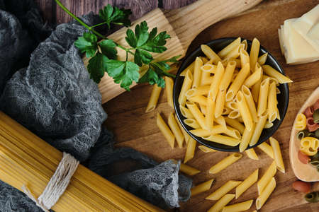 Different raw uncooked Italian pasta and cheese on wooden table. Diet and food concept.の写真素材