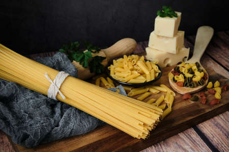 Different raw uncooked Italian pasta and cheese on wooden table. Diet and food concept.の写真素材