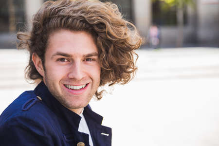 Portrait of happy young man with blonde curly hair and trendy clothes looking at cameraの写真素材