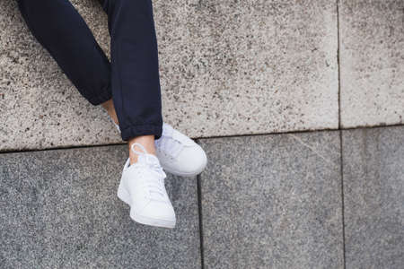 Young fashion man legs with sneakers seated in stone wall. White shoesの写真素材