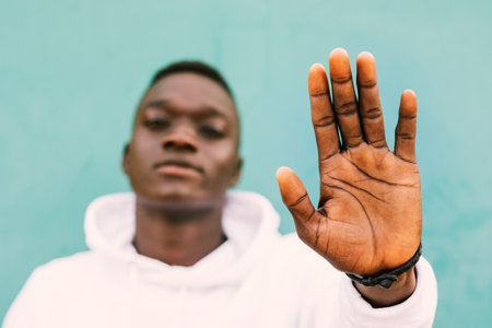 Young african black man against a green wall looking at camera doing a hand stop sign wearing a white sweatshirt with confidence. Selective focusの写真素材