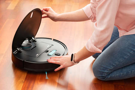Faceless middle section of young woman cleaning the deposit of an automatic vacuum cleaner to clean the floor, opened machine housework robotの写真素材