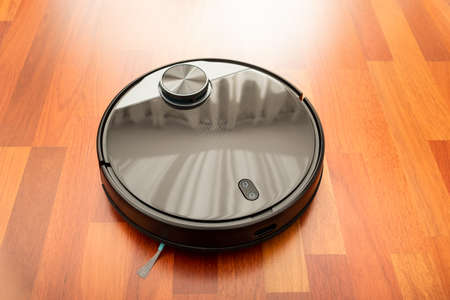 Black automatic vacuum cleaner robot in a house to clean the floor and help in housework. Smart home technology of the future and artificial intelligenceの写真素材