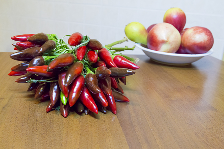 bunch of chillies on wooden kitchen table with dish of peaches and pearsの写真素材