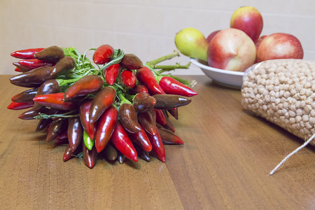 bunch of chillies on wooden kitchen table with dish of peaches and pears and bag of chickpeasの写真素材