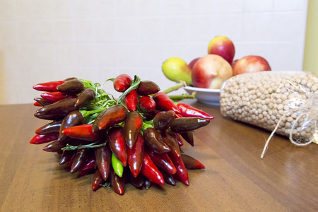 bunch of chillies on wooden kitchen table with dish of peaches and pearsの写真素材