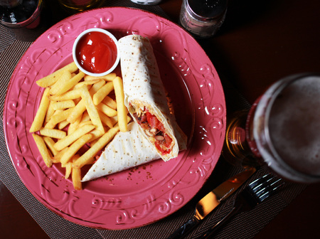 Burrito with French fries, beer, ketchup,  fork, knife on the red plate and napkin.の写真素材