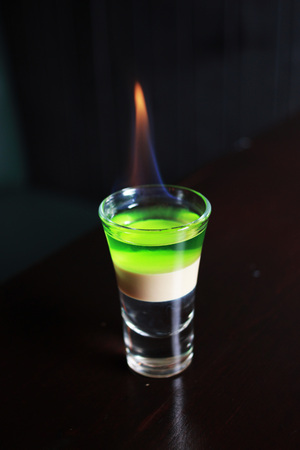 Burning striped multilayer alcohol drink in shot glass on a table. Cocktail with flame.の写真素材