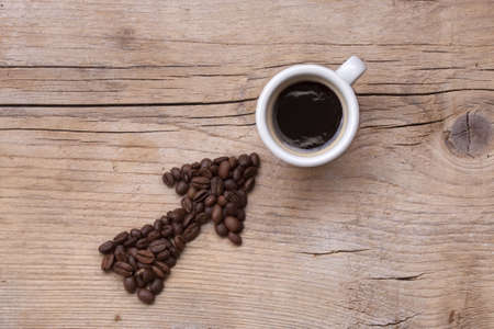 Arrow of coffee beans pointing at a filled coffee cup, all set on an old wooden board, diagonal layoutの写真素材