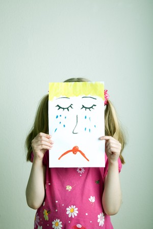 Little blonde girls holding sad face maskの写真素材