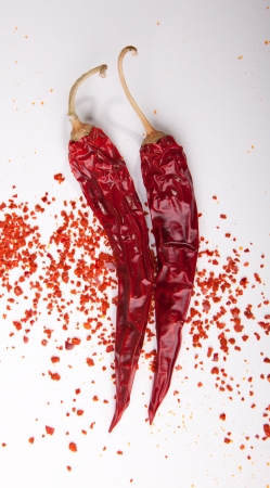 Two dried red hot chili peppers with flakes of grounded peppers