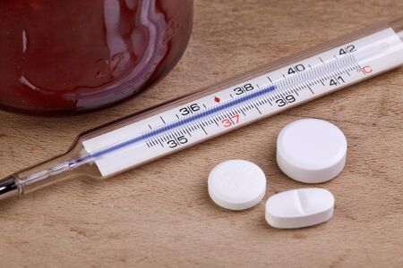 Symbolic image of fever thermometer with conventional pills and household remedys