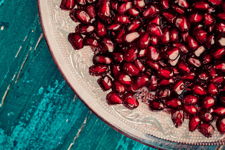 Fresh bright red Pomegranate Grenadine seeds on glass plate on blue wooden backgroundの写真素材