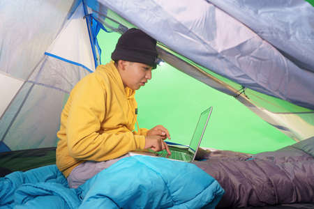 boy playing with a laptop inside a tent on a green backgroundの写真素材