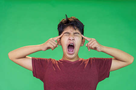 hispanic teenager with acne on his face screaming isolated over green backgroundの写真素材
