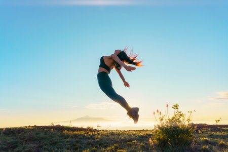 Woman jumping at dawn in mountainの写真素材