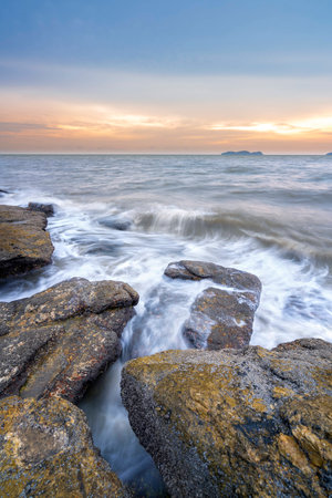 Waves hitting rocks at beach during sunsetの写真素材