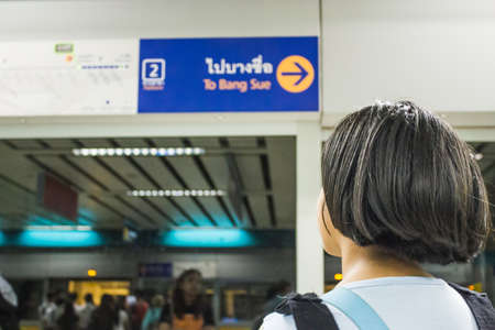 young girl at subway of Thailand, looking at the station signの写真素材