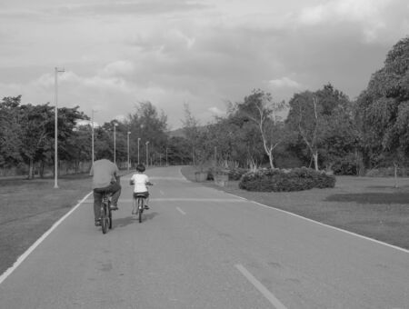 Dad and his daughter riding bicycle in the park of Thailand in black and white tone photoの写真素材