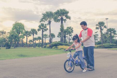 Asian father teach daughter for ride bicycle in the parkの写真素材