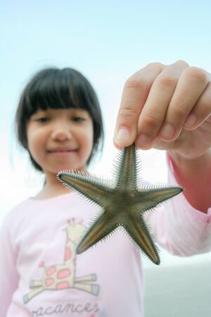 little Asian girl holding starfish at the beachの写真素材