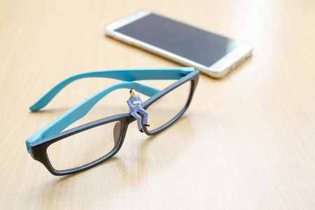 businessman miniature sit on glasses with background of smart phone on wood floorの写真素材