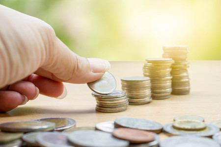 hand saving stack of coins with soft sunlight on green nature background