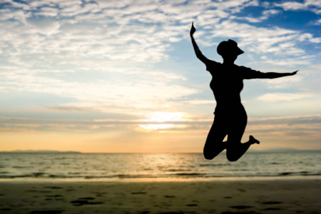 silhouette of happy woman jumping at the sunset beachの写真素材