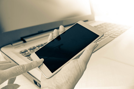 hand use smart phone on blur background of Laptop in sepia filterの写真素材