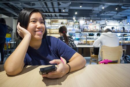 Asian girl using smart phone and smiling in coffee shop