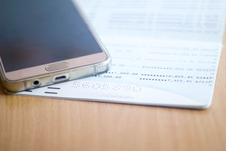 mobile phone with book bank on wood tableの写真素材