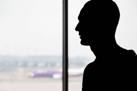 silhouette of sad man at airport ,standing near window and looking at the air planeの写真素材