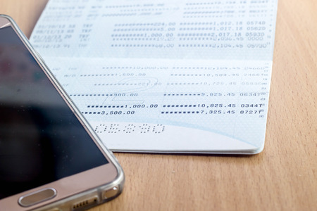 mobile phone with book bank on wood tableの写真素材