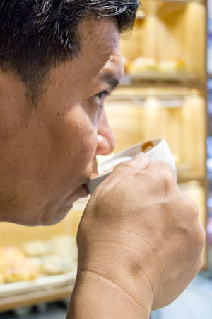 Asian man drinking tee or coffee in white cup