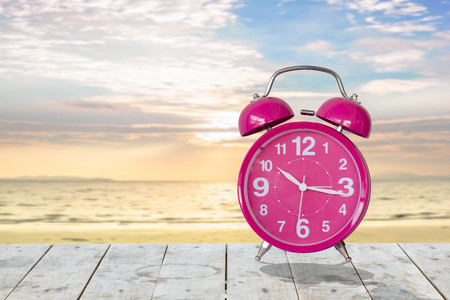 pink alarm clock on wood table with blur background of the beachの写真素材