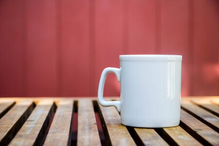 white coffee mug on wood table with red backgroundの写真素材
